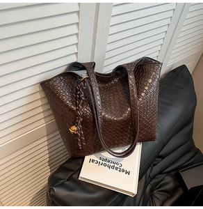Detail of dark brown tote bag featuring woven texture and decorative golden charm