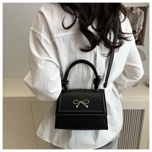 Detalle del bolso bandolera negro con broche de lazo dorado y asa anudada