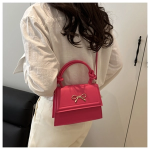 Bolso bandolera rosa chic con lazo dorado mostrado en modelo con ropa blanca