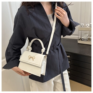 Detalle de bolso cuadrado blanco con lazo dorado y asa anudada llevado por modelo