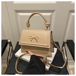 Detalle de bolso cuadrado beige con hebilla de lazo dorado y asa con nudo chic