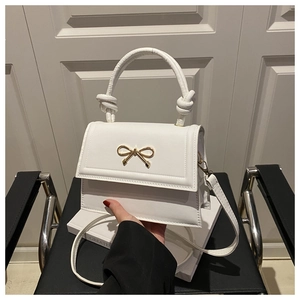Detalle de bolso blanco de cuero PU con lazo dorado y asa decorativa anudada