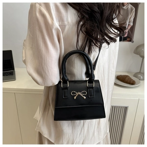 Detail of a black leather handbag with a golden metal bow shown in a modern lifestyle setting