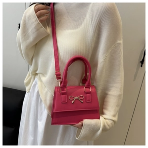 Detail of magenta mini handbag featuring a gold bow buckle and adjustable shoulder strap
