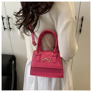 Detailed view of a pink structured handbag featuring a gold bow accent and PU material