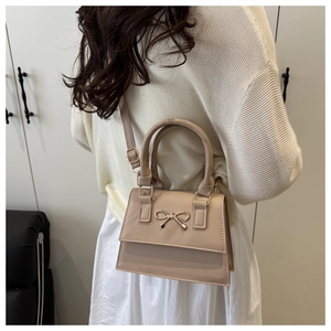 Detail of a beige flap bag with a metal bow accent shown on a model for a chic look