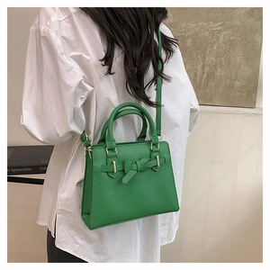 Groene trapeziumvormige handtas met goudkleurige hardware en strik gedragen over de schouder