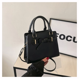 Détail d'un sac à main noir avec noeud et finitions dorées sur étagères blanches