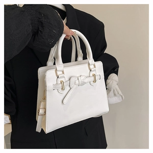 Detail van een witte gestructureerde handtas met decoratieve strik en gouden hardware