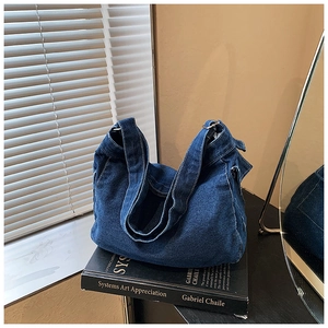 Dettaglio borsa tote in denim blu scuro con bordi sfrangiati su un libro d'arte