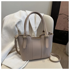 Detail view of a beige leather bucket bag on a chair with visible stitching and handle