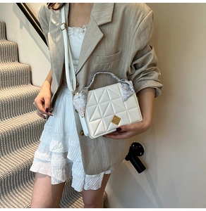 Détail d'un sac matelassé blanc avec boucle dorée et foulard en soie enroulé sur la poignée
