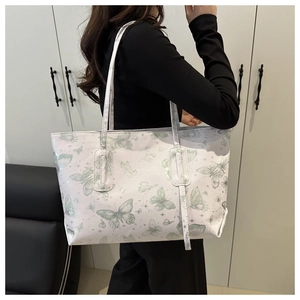 Modern white tote bag with green butterfly print shown on shoulder in a lifestyle setting