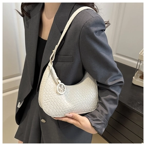 Detailaufnahme einer weißen gewebten Schultertasche mit M-Anhänger an einem Model