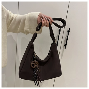 Detail of dark brown crescent bag featuring a pretzel charm and striped tassel accent
