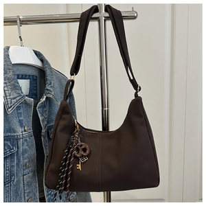 Close-up of deep brown hobo bag with matte finish and woven pendant on a metal hanger