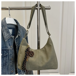 Detail of sage green crescent tote bag with brown tassel and wooden ring on denim jacket