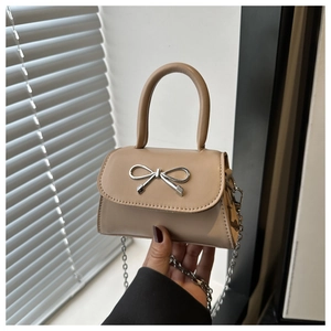 Detail of elegant beige crossbody bag with silver bow buckle and metal chain strap