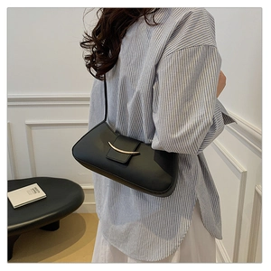 Detail shot of a black leather shoulder bag with a crescent gold buckle on a model