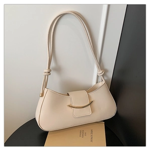 Detailed shot of cream leather baguette bag featuring a gold crescent buckle and knotted strap