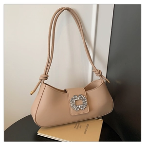 Detail of beige leather shoulder bag with crystal buckle and knotted strap on a table