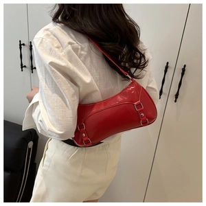 Model wearing a red patent leather underarm bag with decorative metal buckle straps