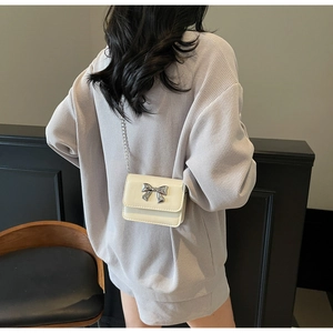 Détail d'un mini sac bandoulière blanc crème avec nœud en métal argenté et bandoulière chaîne