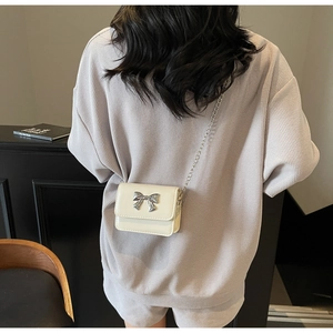 Detail of a white mini crossbody bag with a silver metal bow and thin chain strap
