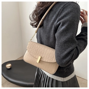 Detail der beigen Tasche in Krokoprägung mit goldener Schnalle und Kette am Model