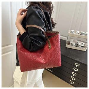 Detail of red woven tote bag with slim brown handles and gold rivet hardware accents