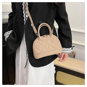 Borsa beige a conchiglia trapuntata indossata da modella con blazer nero e vestito bianco