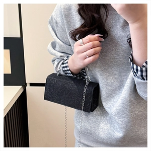 Close-up of a sparkling black glitter clutch bag with silver chain strap held by model