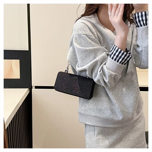 Detailed view of shimmering black glitter clutch with silver chain strap worn by a model