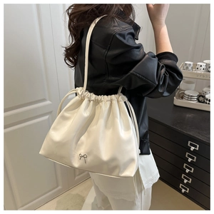 Close-up of white glossy pleated shoulder bag with a metallic bow worn by a model