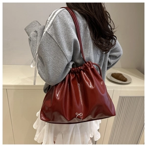 Detail of burgundy glossy leather bucket bag with drawstring and silver bow pendant