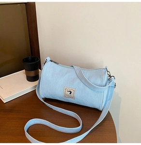 Detail of light blue denim barrel bag featuring a cute cartoon dog patch and zipper