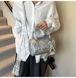 Detail showing the silver textured cylinder bag with pearl bow charm and shoulder strap