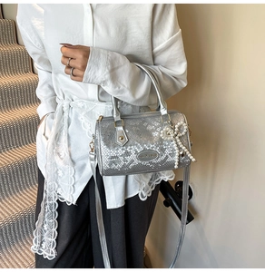Close-up of silver snake pattern Boston bag with pearl bow charm worn by a model
