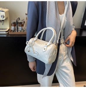 Detail of white embossed cylinder boston bag with pearl bow charm and shoulder strap