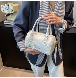 Detail view of white snakeskin texture Boston bag with pearl bow and metal heart charm