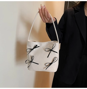 Detail of off-white leather bucket bag with four black bows held by a model