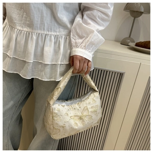Close-up of butterfly embroidery and golden glitter details on cream shoulder bag