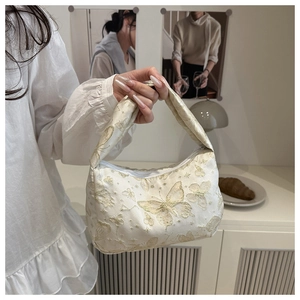 Detailed shot of cream shoulder bag with golden butterfly embroidery and chain strap