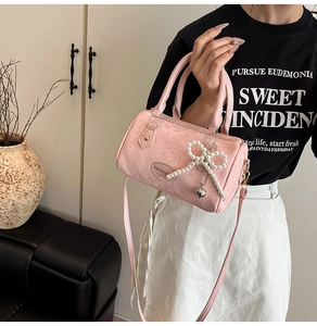 Detailed shot of pink textured mini Boston bag with pearl bow charm and shoulder strap