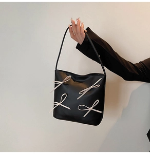 Detail of black matte leather tote bag featuring four pink balletcore style ribbons