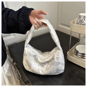Detail of white satin shoulder bag with silver butterfly print and metal zipper closure