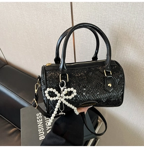 Detailed view of black snake-textured boston bag with pearl bow charm and top zip