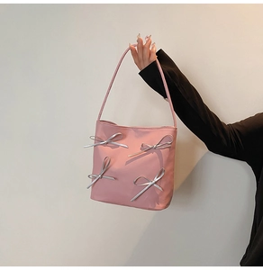 Detailed shot of pink bucket bag featuring 3D silver bow accents and long handles