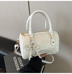 Detail of white snakeskin texture Boston bag with pearl bow charm and logo plate