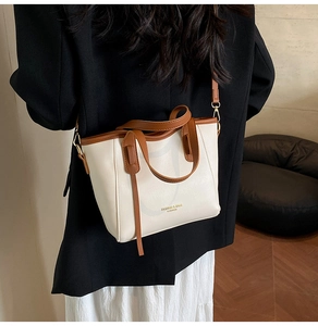 Dettaglio della borsa tote beige con manici marroni indossata da modella in blazer nero